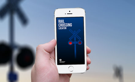 Gros plan d'un smartphone affichant le localisateur de passages à niveau. L'arrière-plan est une image floue d'un passage à niveau.