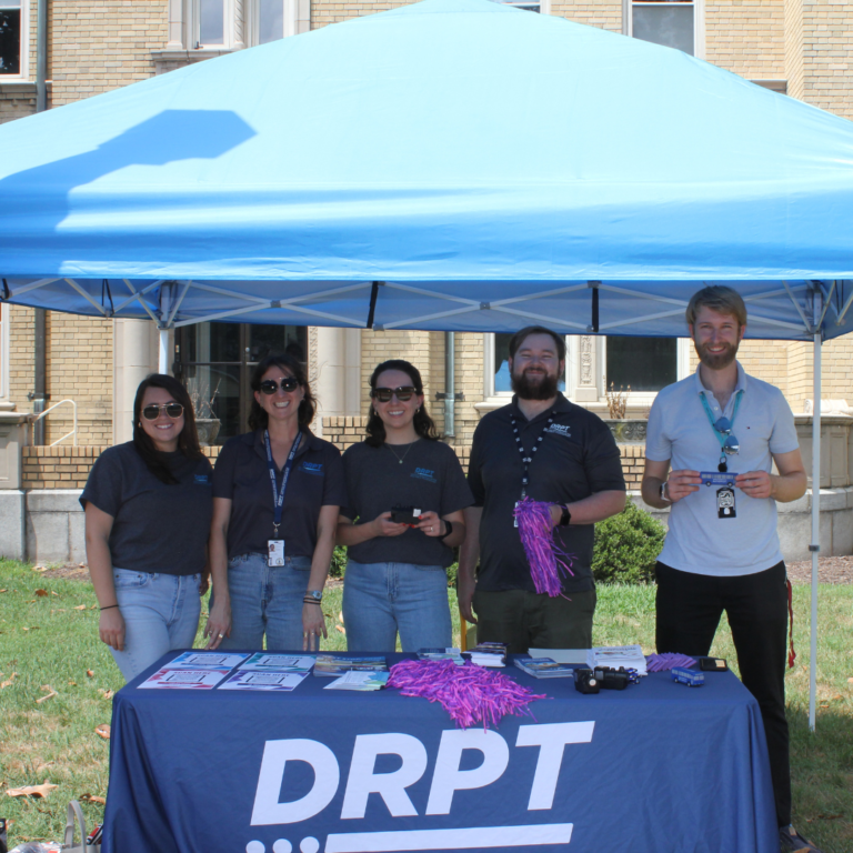 Le personnel de DRPT tient des articles promotionnels à la table de marque de DRPT sous la tente bleue